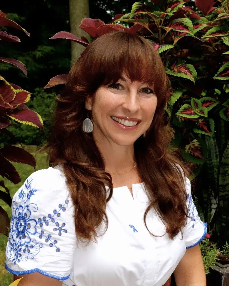 Jill, founder of JEA Strategies, smiling among garden foliage